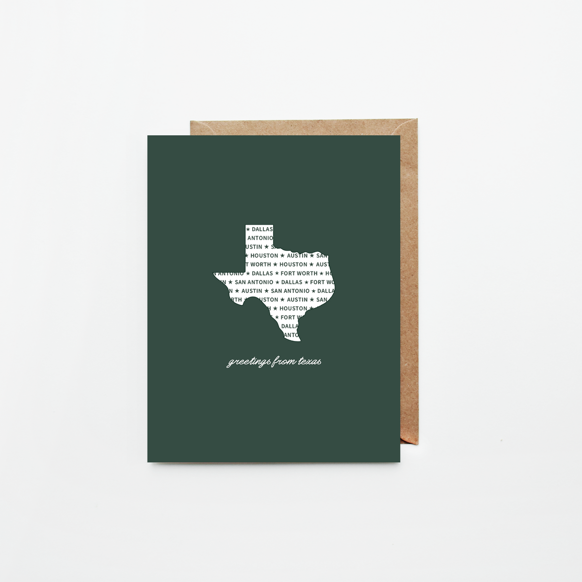 A dark green greeting card featuring a white silhouette of Texas filled with text, with the phrase 'greetings from Texas' printed below, shown with a brown kraft envelope on a light gray background.