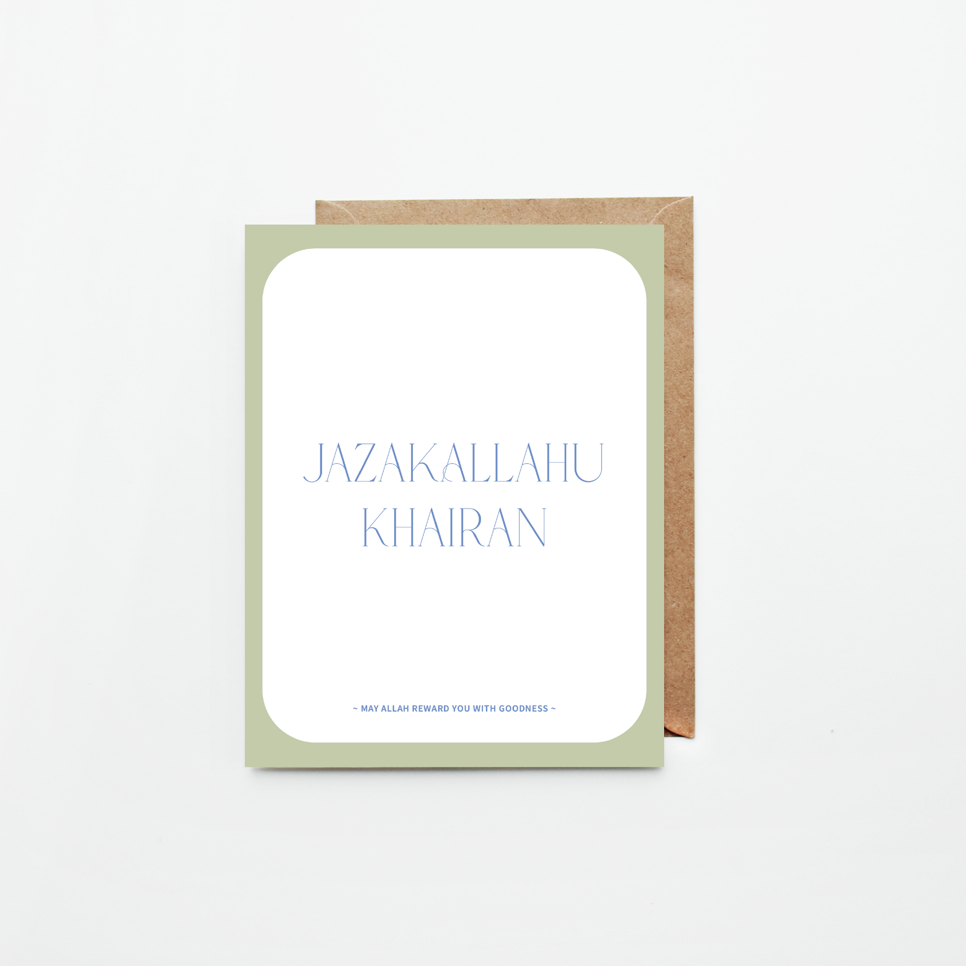 A greeting card with a white center panel, pale sage green border, and blue text reading 'JAZAKALLAHU KHAIRAN' with smaller text below, shown with a brown kraft envelope on a light gray background.